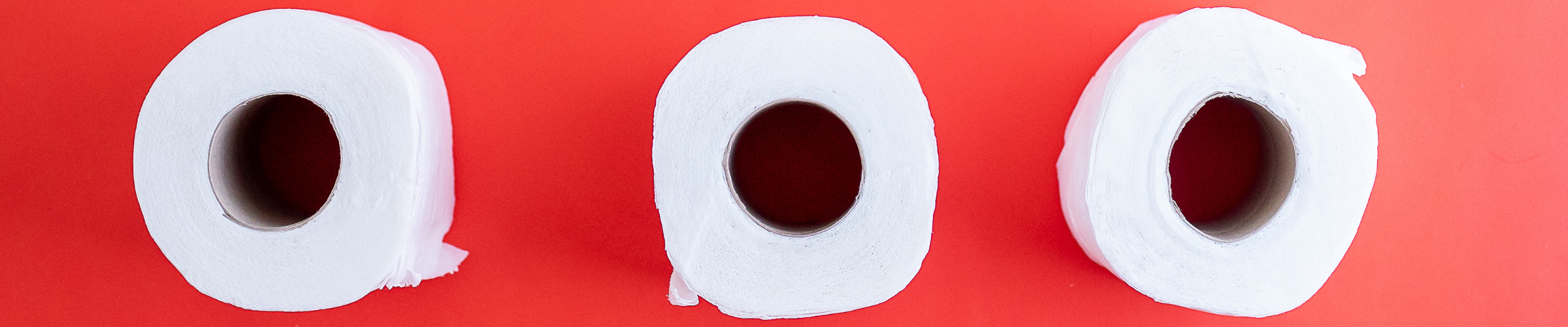 three toilet paper rolls seen from the top. they sit side by side on a red background.